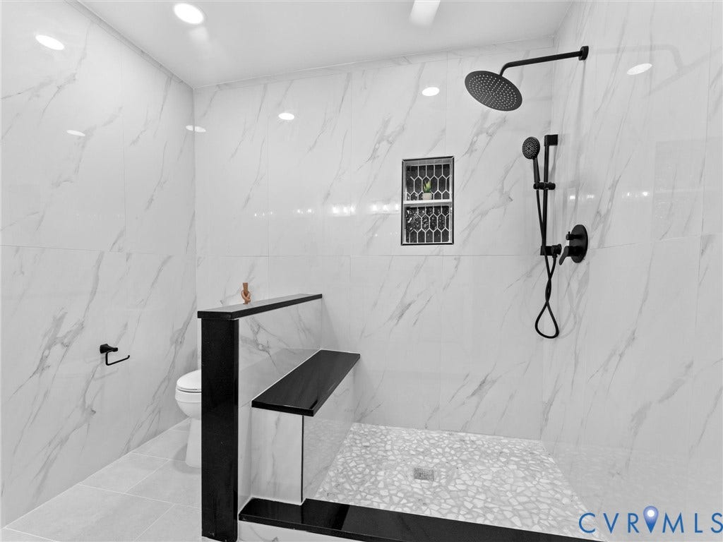 Spacious shower with large format white tile walls, rain shower head, handheld shower fixture, built-in niche, and mosaic tile shower pan