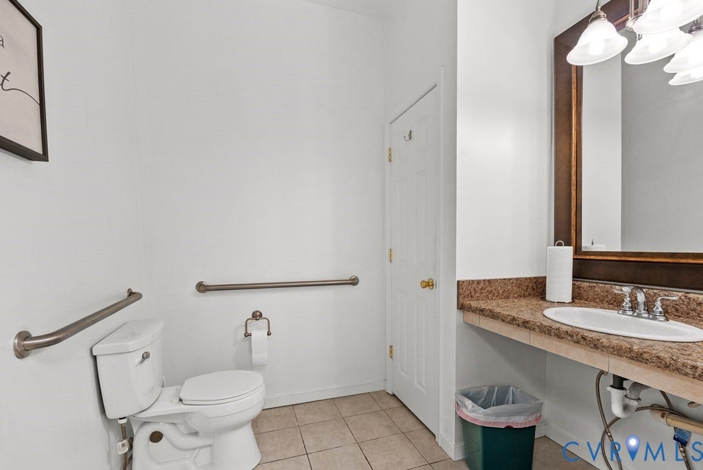 White-paneled door, tile flooring, stone-finish countertop, single basin sink, and framed mirror with integrated lighting