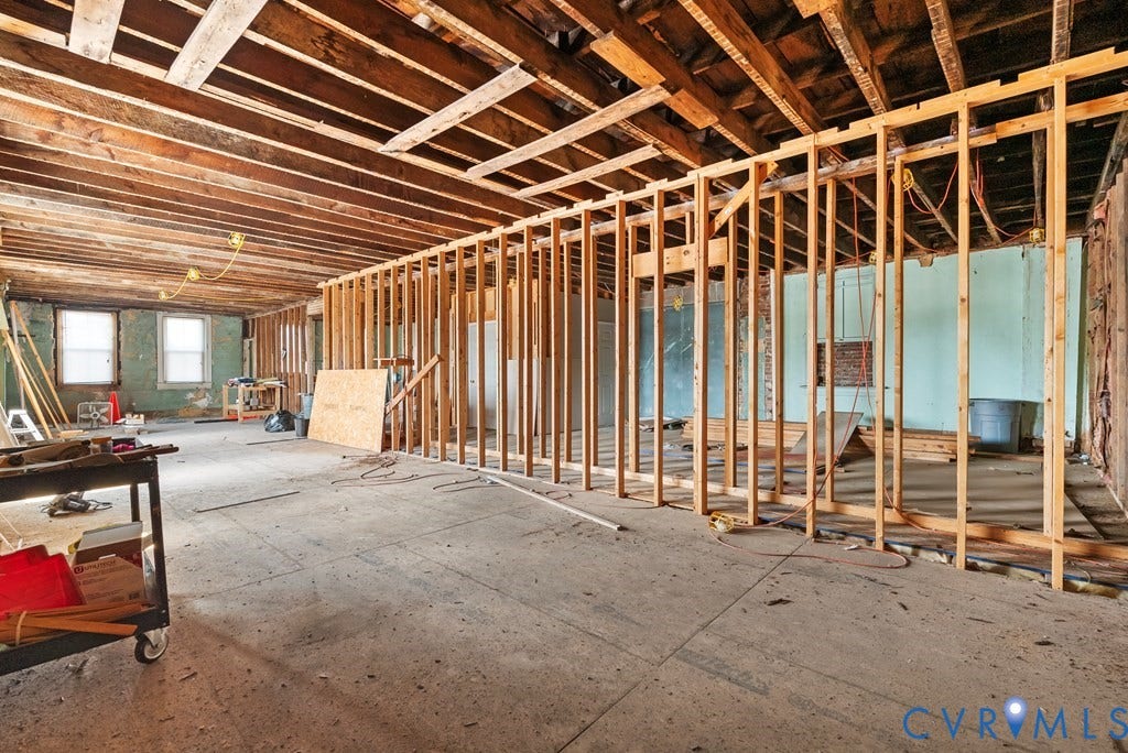 Exposed wooden ceiling joists and wall studs define this space, featuring multiple windows and an open floor plan ready for customization