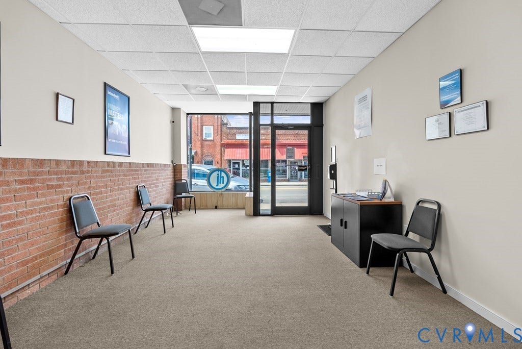 Commercial entry with full-light glass door, large storefront window, drop ceiling with recessed lighting, and a brick accent wall