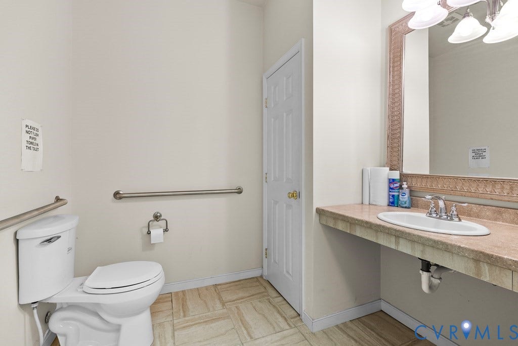 Tile flooring, wall-mounted grab bars, toilet, vanity with integrated sink, and an ornamental framed mirror