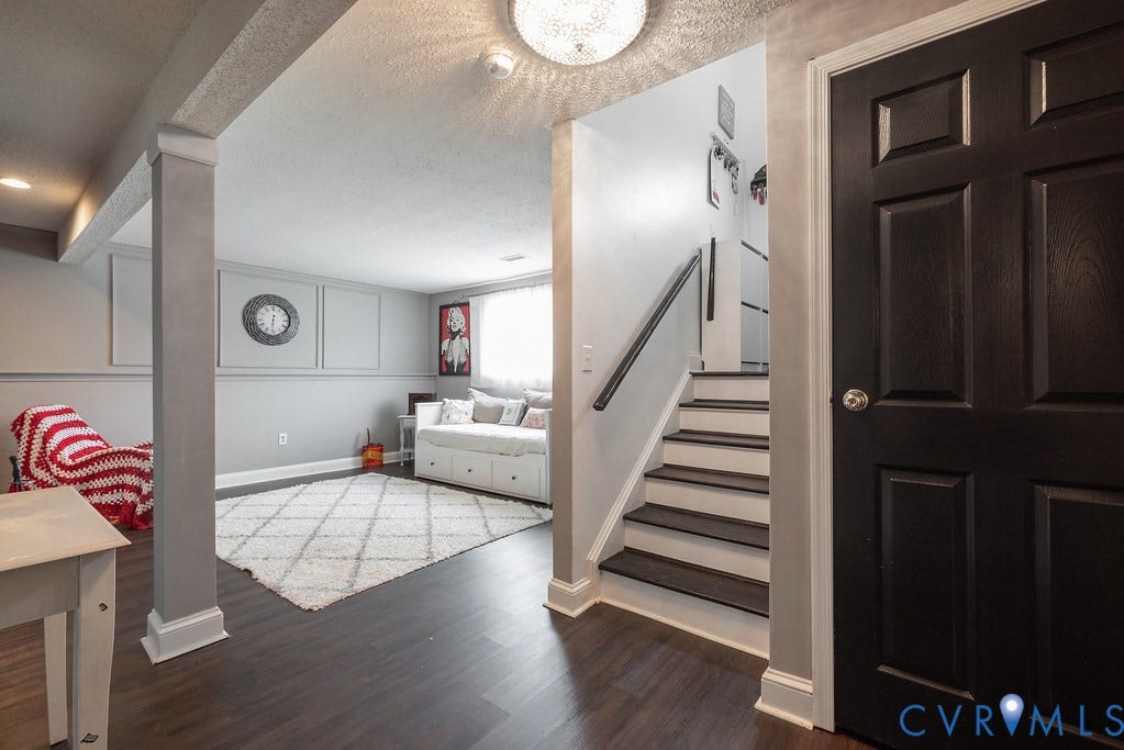 Wood-finish flooring throughout, white baseboards, and a staircase with dark treads and white risers