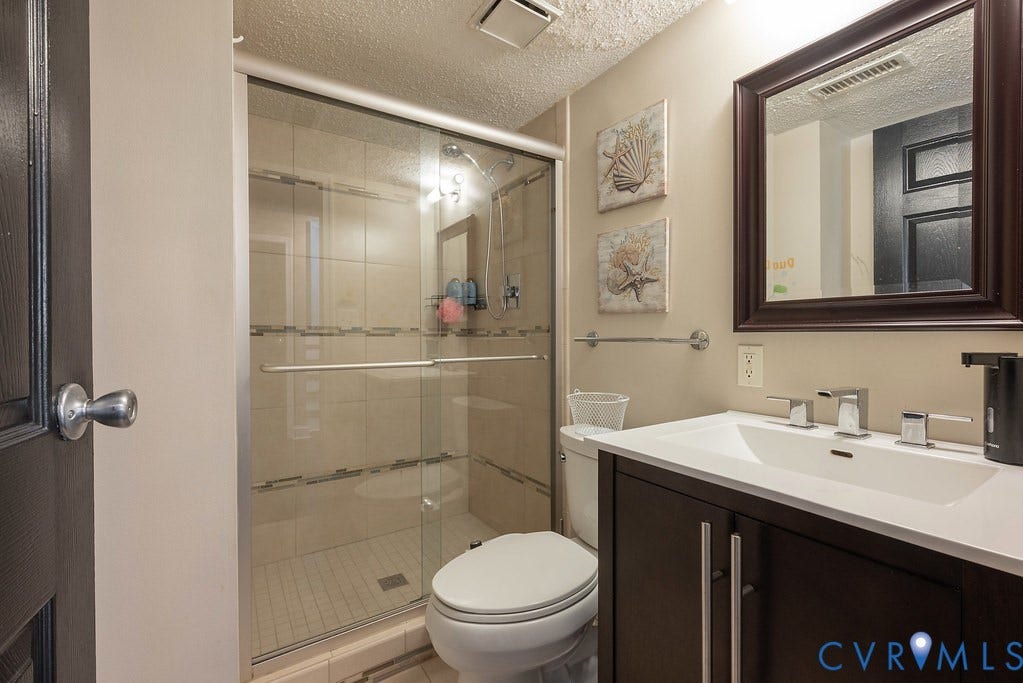 Glass-enclosed shower with tiled walls and floor, vanity with an integrated sink, dark wood-finish cabinetry, and a framed mirror