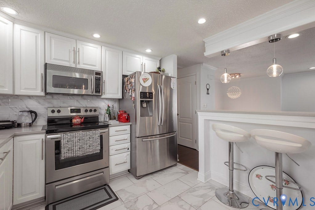 White shaker-style cabinetry, stainless steel dishwasher, undermount sink with a gooseneck faucet, light-toned countertops, and marble-look tile flooring