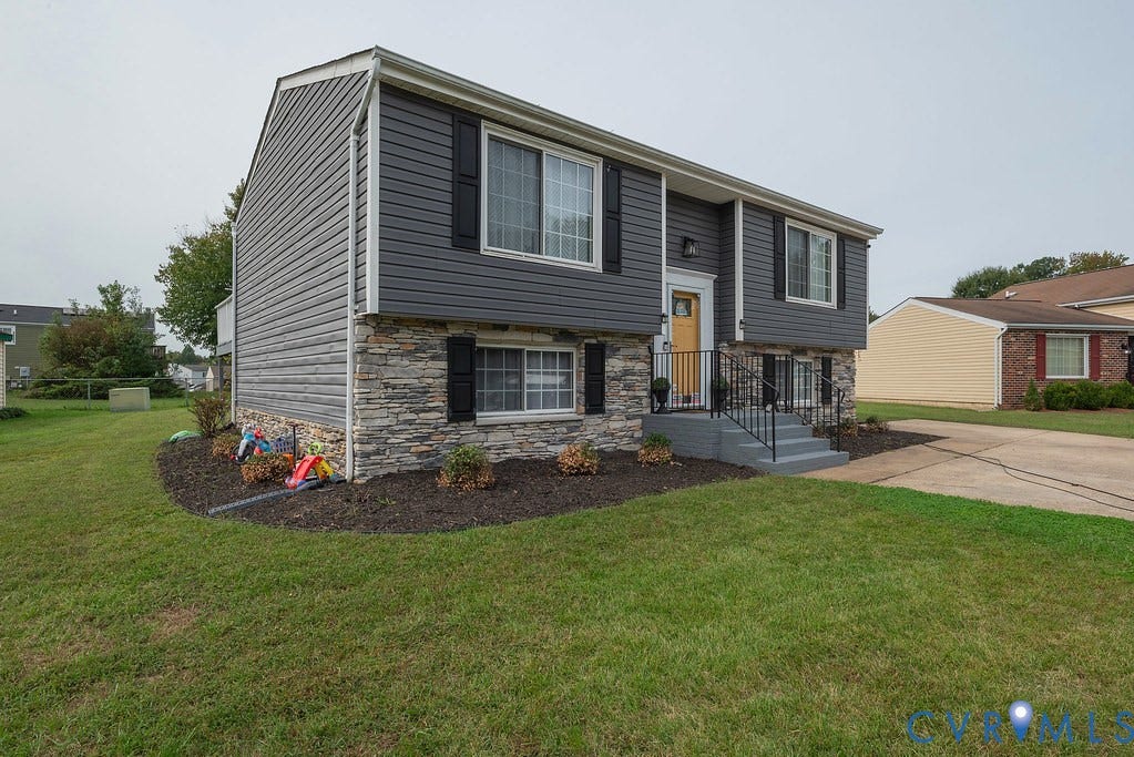 Split-level exterior featuring gray siding, stacked stone facade, and a yellow entry door