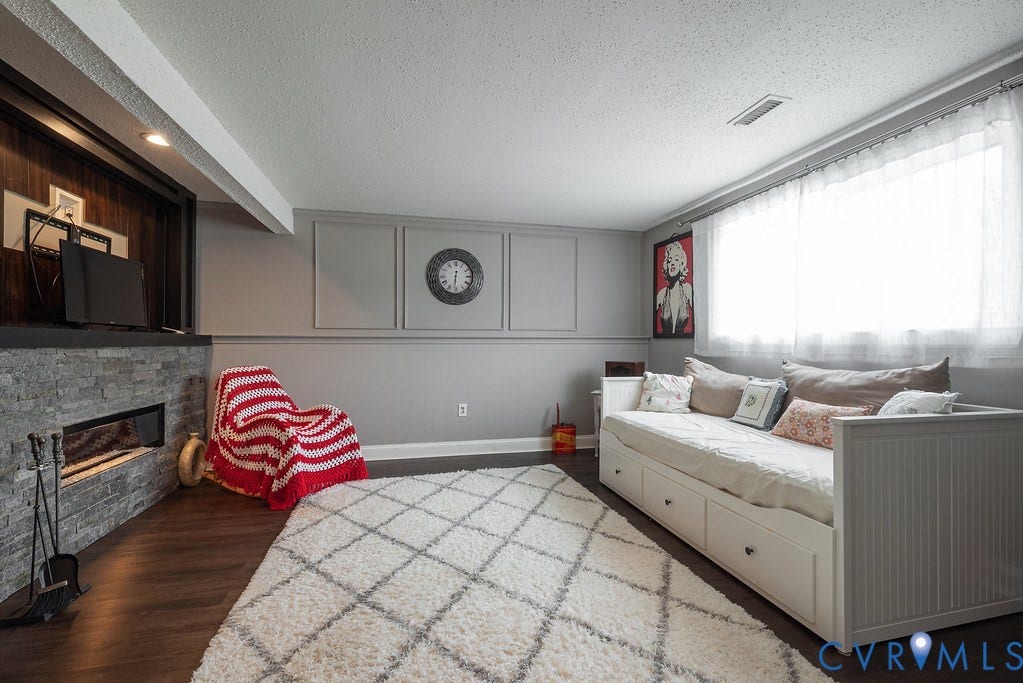 Built-in fireplace with stone-finish surround, wood-finish flooring, recessed lighting, and a window with sheer curtains