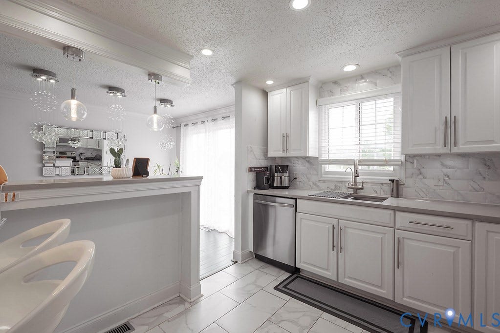 White cabinetry, marble-patterned tile backsplash, stainless steel sink, brushed nickel faucet, and integrated stainless steel dishwasher