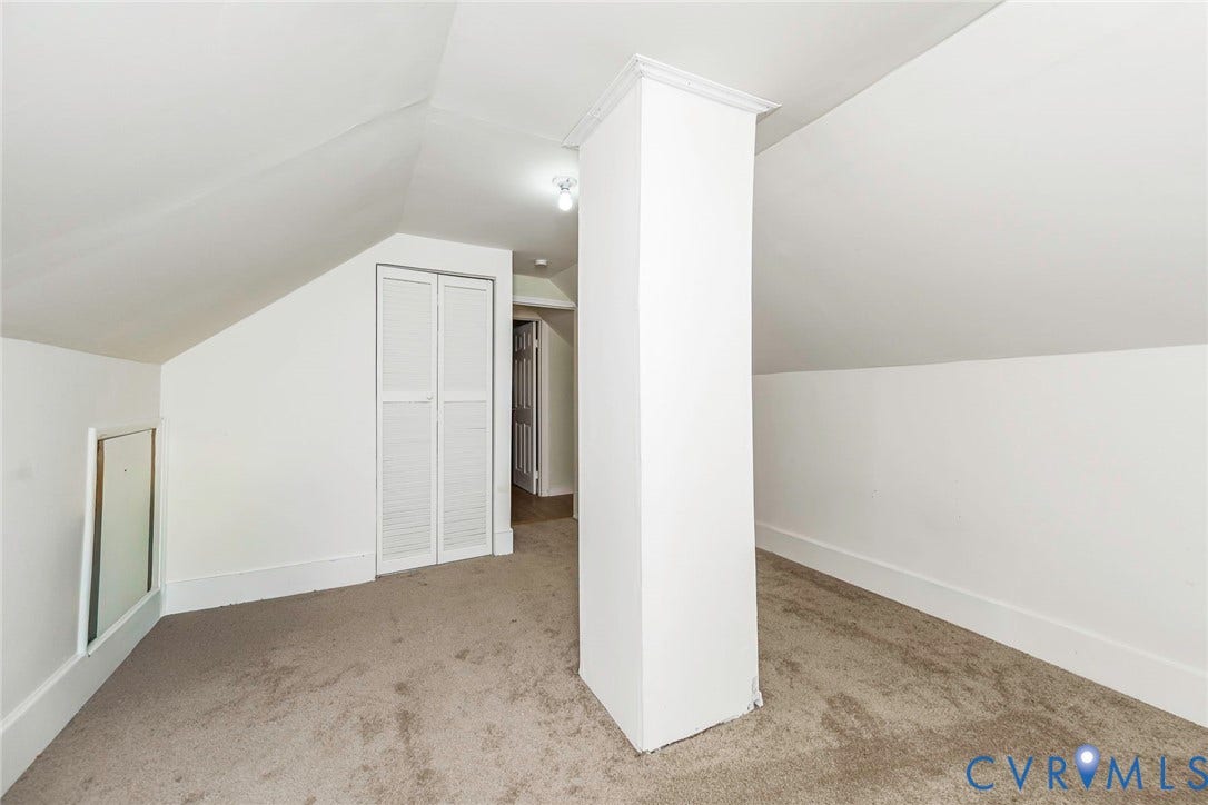 Carpeted attic space featuring sloped ceilings, a closet with bi-fold louvered doors, and white painted walls