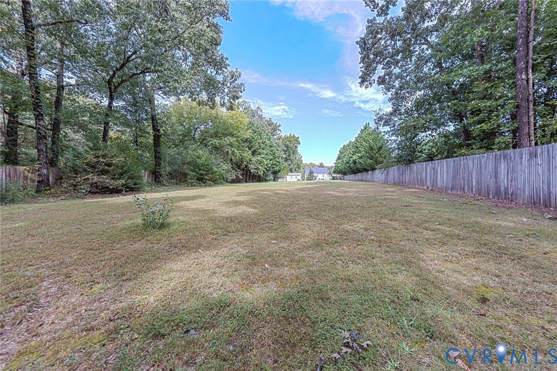 Expansive grassy lot bordered by mature trees and a wood fence