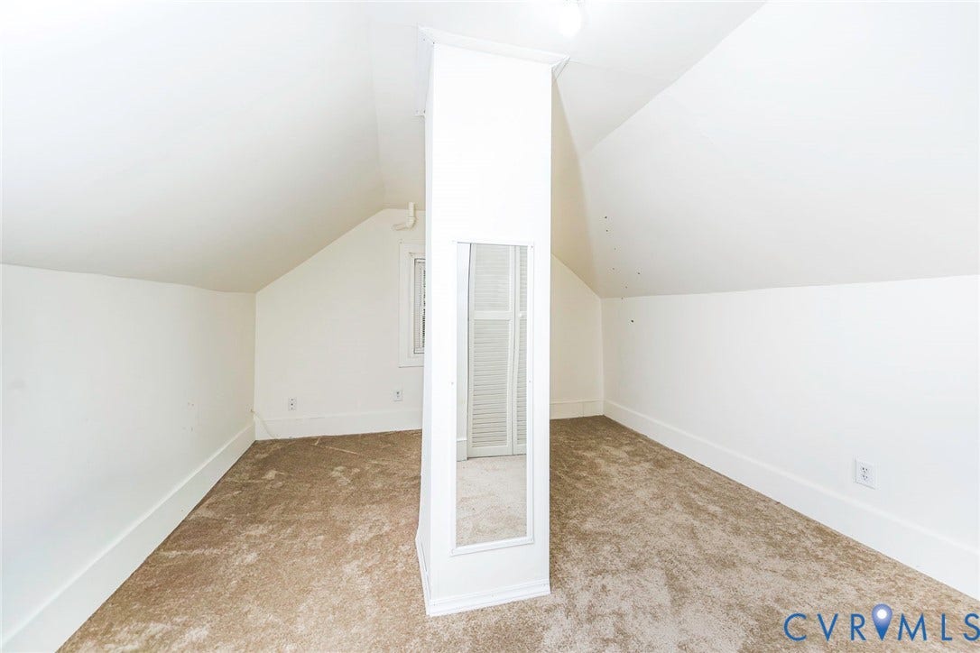 Carpeted attic space with sloped ceilings, white walls, and a window
