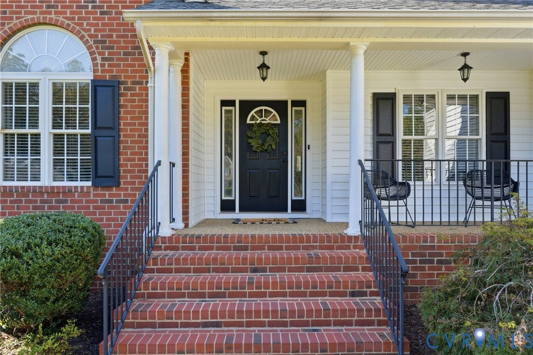 11813 Longfellow Drive, Bayhill Pointe, Midlothian, VA 23112 Covered front porch featuring red brick steps, white support columns, black metal railings, and a front entry door with a decorative transom window
