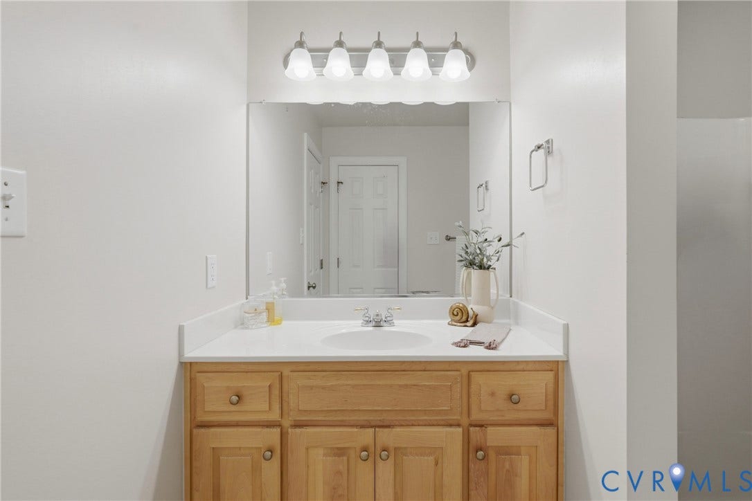 11813 Longfellow Drive, Bayhill Pointe, Midlothian, VA 23112 Single-basin vanity with a solid-surface countertop, natural wood cabinetry, large wall-mounted mirror, and five-light vanity fixture