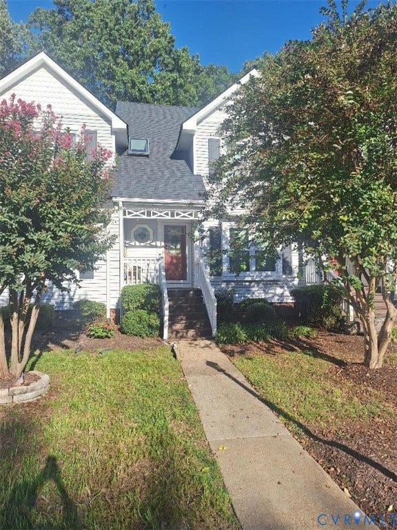 Gabled roofline with a skylight, white siding exterior, covered porch with decorative railing, red entry door, and a concrete walkway