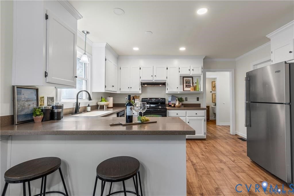 White cabinetry with dark hardware, stone-finish countertops, wood-finish flooring, stainless steel refrigerator, and recessed lighting