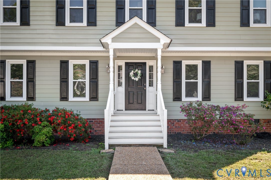 Siding exterior with black shutters, brick foundation, and a covered entry porch