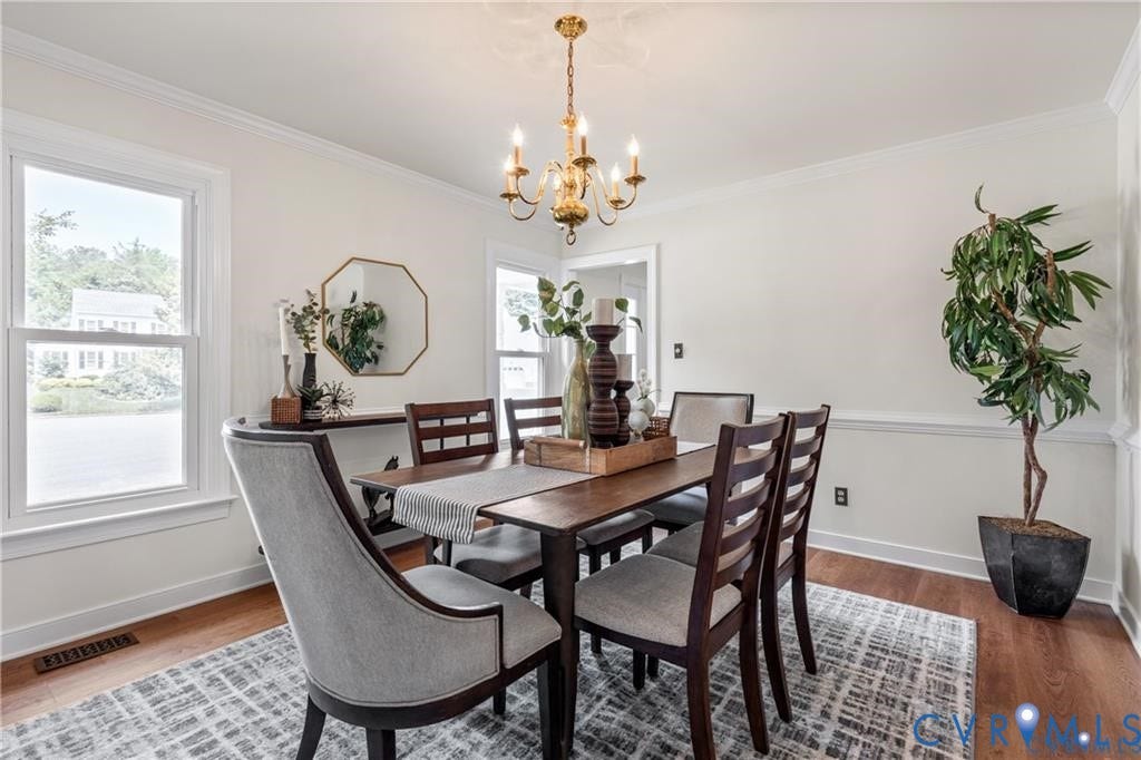 Hardwood flooring, crown molding, white trim, recessed panel wainscoting, and a brass chandelier