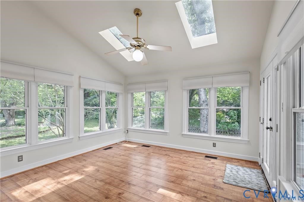 Vaulted ceilings with two skylights, multiple double-hung windows, wood-finish flooring, and a ceiling fan with integrated lighting