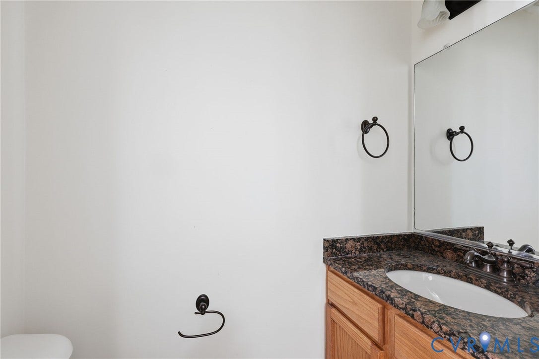 2803 Queensland Drive, #2803, Pemberton Oaks, Glen Allen, VA 23294 Bathroom vanity featuring a stone-composite countertop, undermount sink, dual-handle faucet, wood cabinetry, and a full-width wall mirror
