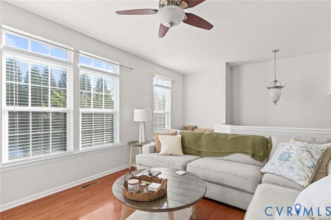 Hardwood flooring, white walls, multiple windows with blinds, ceiling fan, and a pendant light fixture