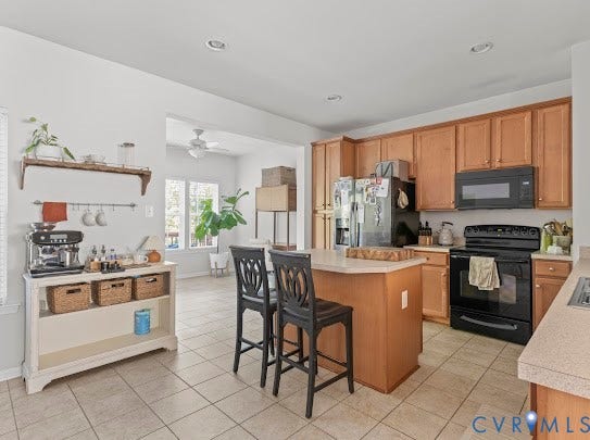 Kitchen featuring wood-finish cabinetry, black appliances, a central island, and tiled flooring