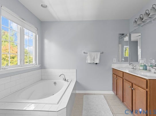 Soaking tub with white subway tile surround, double vanity with wood-finish cabinetry, dual undermount sinks, and tiled flooring