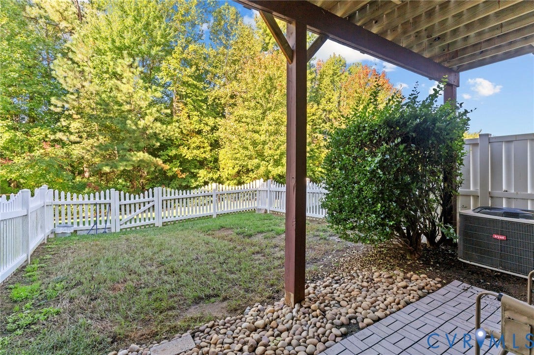 Expansive outdoor space featuring a white picket fence, mature trees, and a paved patio area