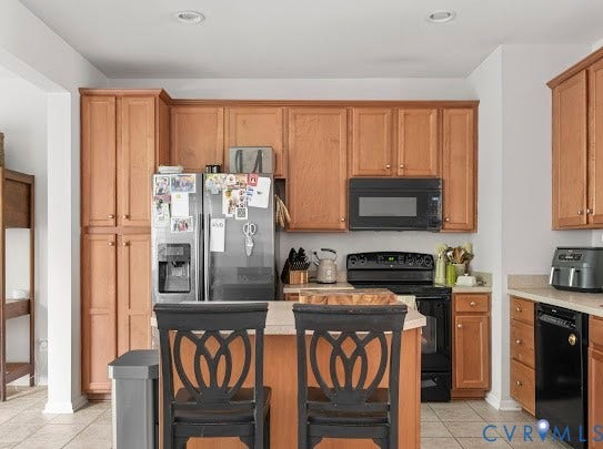 Kitchen featuring recessed lighting, wood-finish cabinetry, black appliances, a stainless steel refrigerator, and a kitchen island with seating