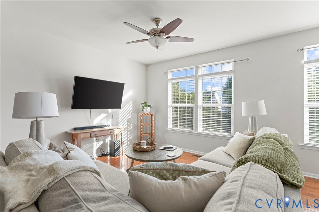 Hardwood flooring, white walls, ceiling fan, and multiple windows with blinds