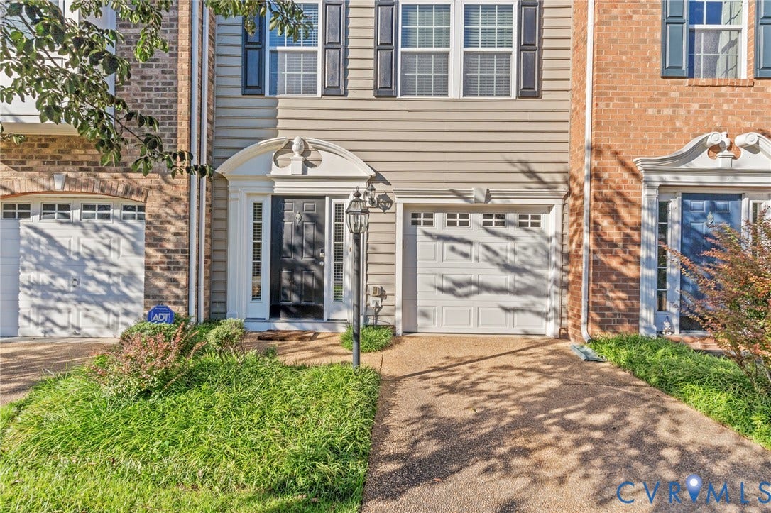 Siding exterior with a decorative portico, black paneled front door, an attached garage, and a lamppost