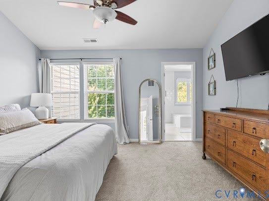Carpeted flooring, ceiling fan, white window blinds, and an open doorway revealing a tiled bathroom with a window