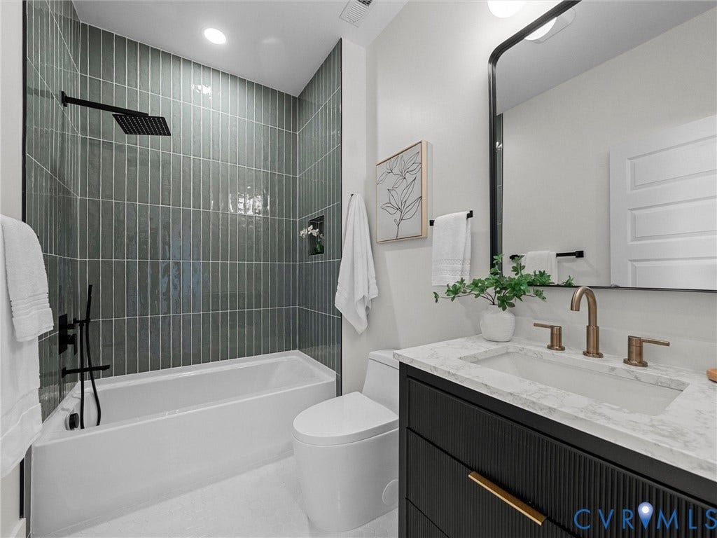 2202 3rd Avenue, Northside, Richmond, VA 23222 Bathroom featuring a soaking tub with dark green vertical tile surround, a sleek black vanity with reeded detailing, a white integrated sink, and bronze-finish fixtures