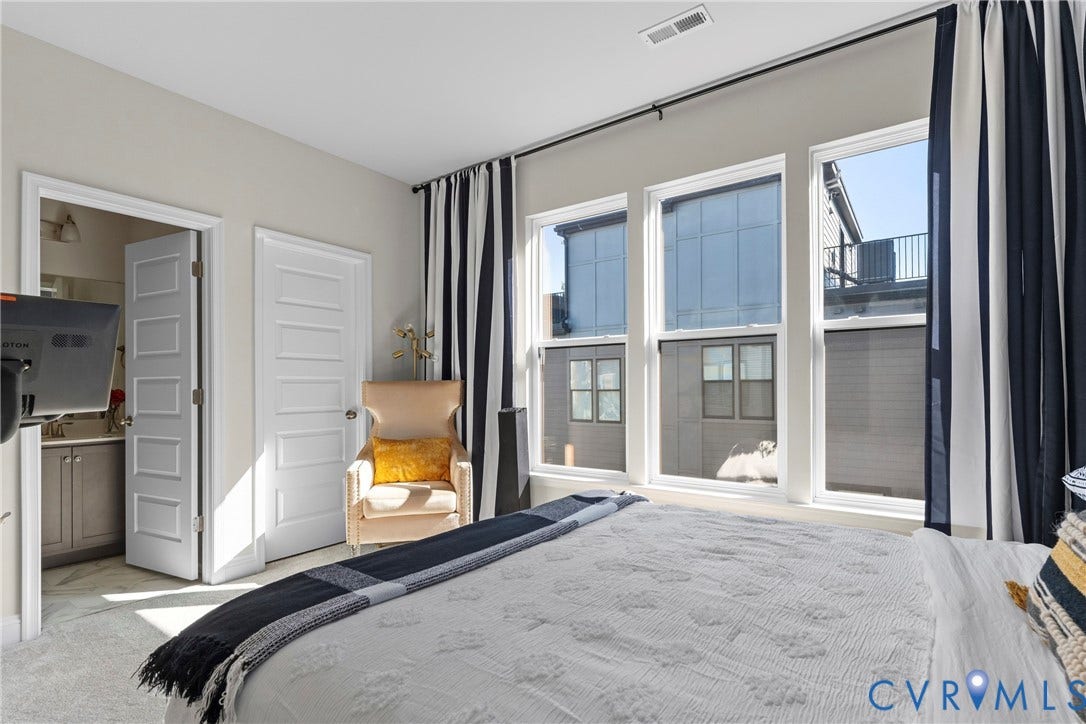 Bright primary bedroom featuring expansive glass doors opening to a private balcony, soft natural light throughout, light wood-finish flooring, and direct access to an en-suite bathroom