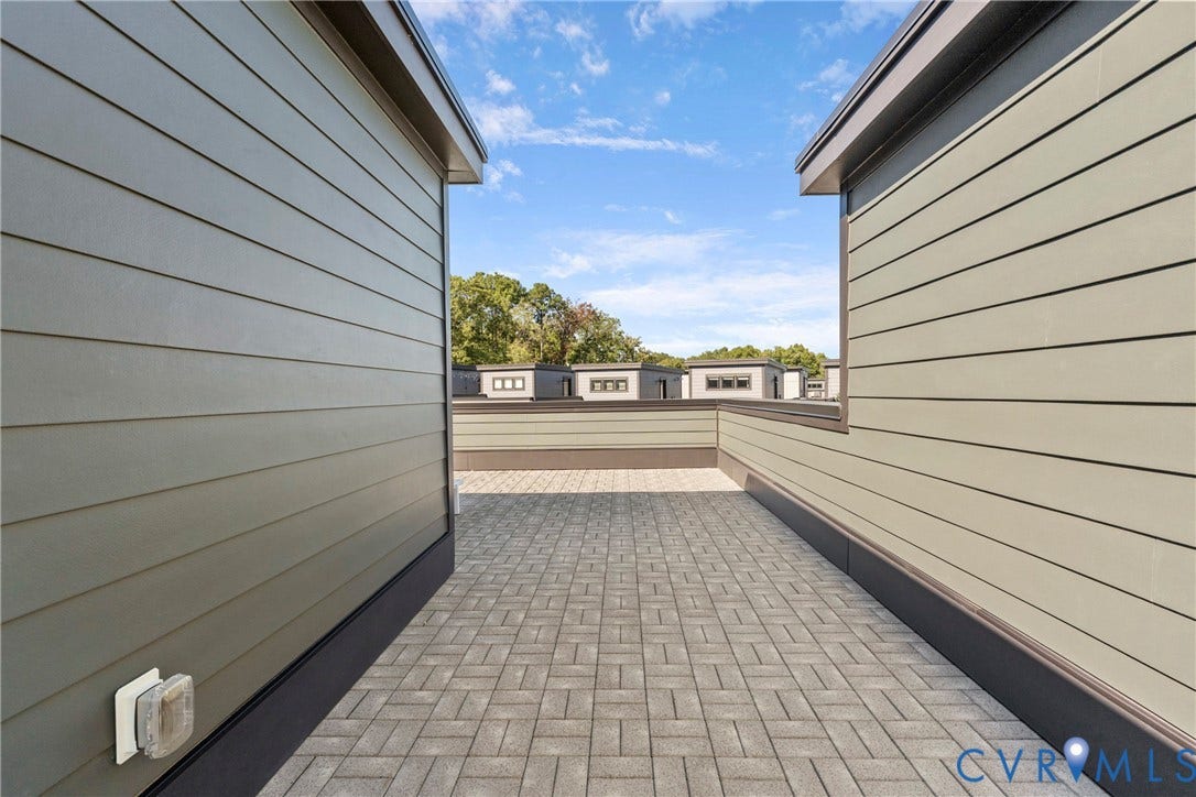 Paved outdoor patio area with gray pavers, surrounded by horizontal siding, and a partial low wall