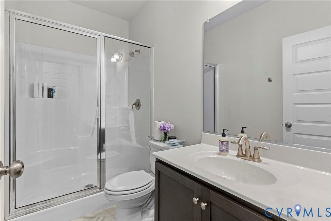 Glass-enclosed shower with white surround, single-basin vanity with a white countertop, dark wood-finish cabinetry, and a large wall-mounted mirror