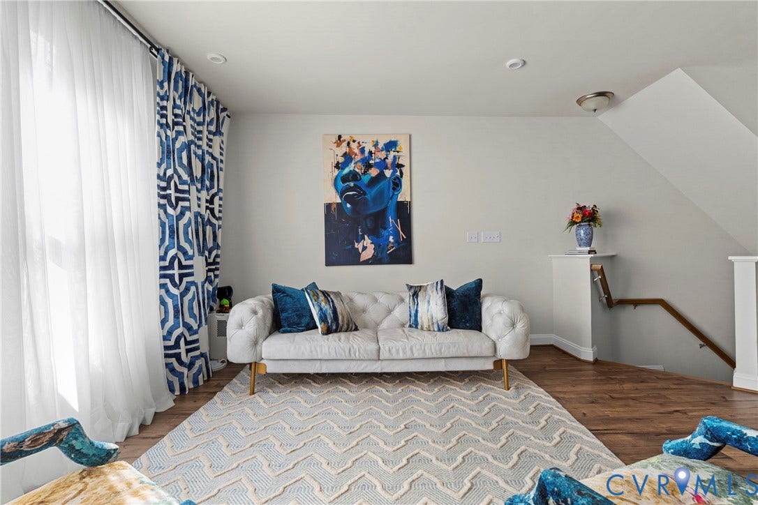 Hardwood flooring, recessed ceiling lighting, light-colored walls, white window sheers, and a built-in stairwell with wood handrail