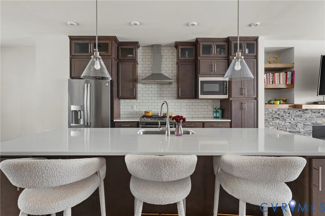 Kitchen featuring a large island with a white countertop, dark wood-finish cabinetry, stainless steel appliances, and subway tile backsplash