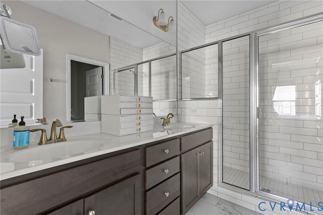 Dual vanity with integrated sinks, brushed brass fixtures, dark wood-finish cabinetry, and a glass-enclosed shower with subway tile surround