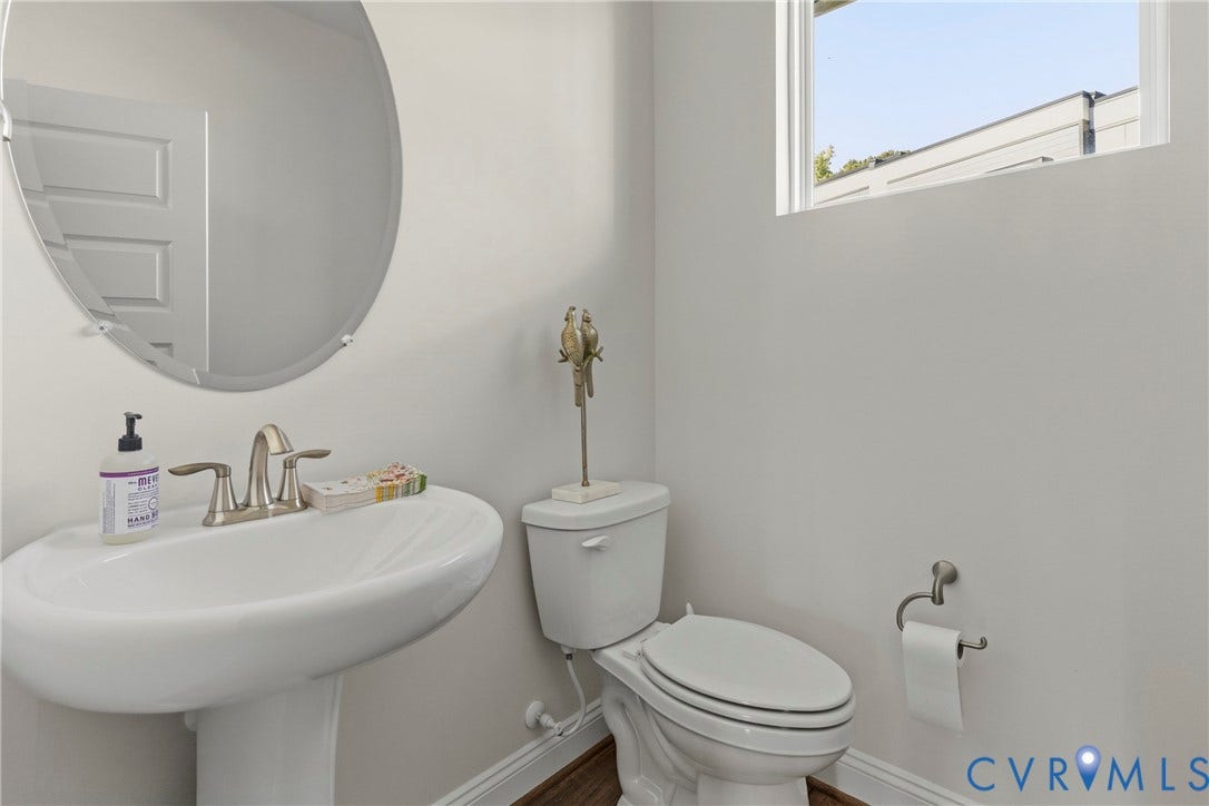Pedestal sink with brushed nickel faucet, circular frameless mirror, and transom window