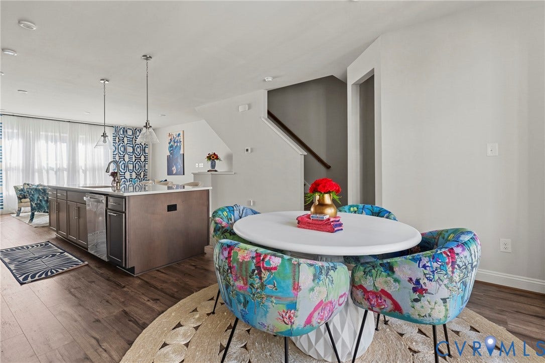 Open-concept living space featuring wood-finish flooring, a kitchen island with integrated sink, pendant lighting, and a visible staircase