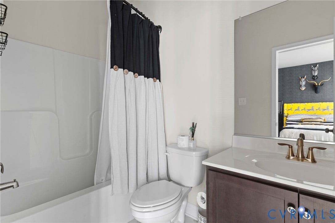 White integrated bathtub with shower, dark wood-finish vanity with a white countertop, and a bronze-finish faucet