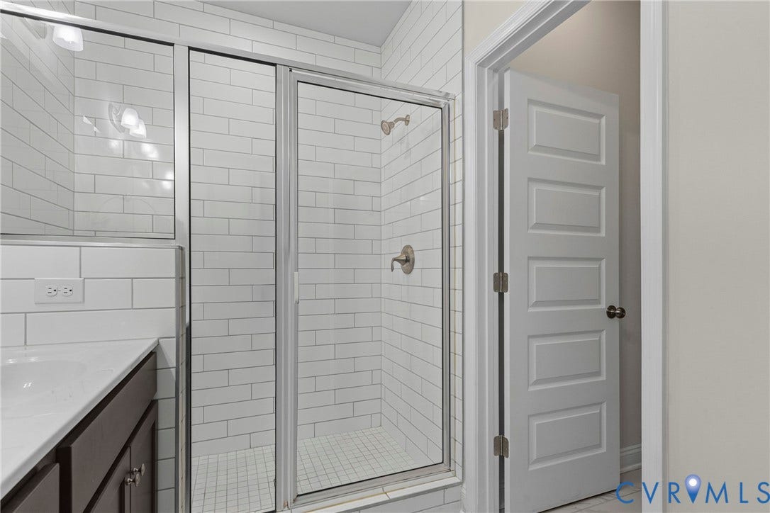 Master bathroom featuring a frameless glass-enclosed shower with subway tile surround, dual vanity with dark wood cabinetry, quartz countertop, and brushed nickel fixtures