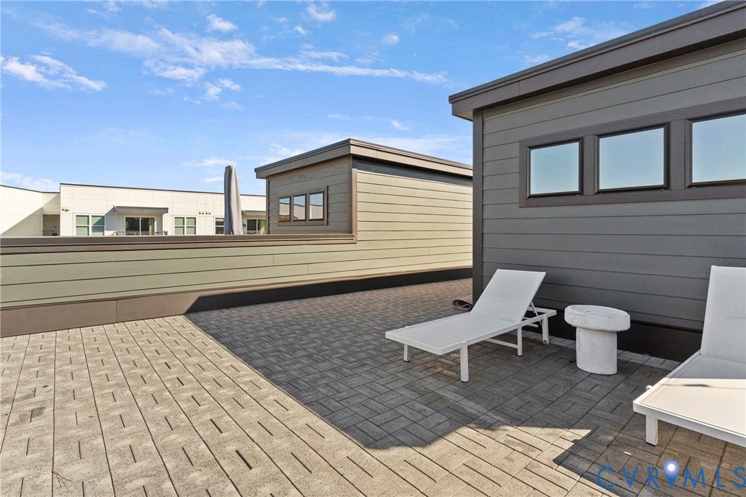 Expansive rooftop terrace featuring mixed-material hardscaping with wood-finish and dark pavers, modern lounge seating areas, and panoramic sightlines across neighboring properties