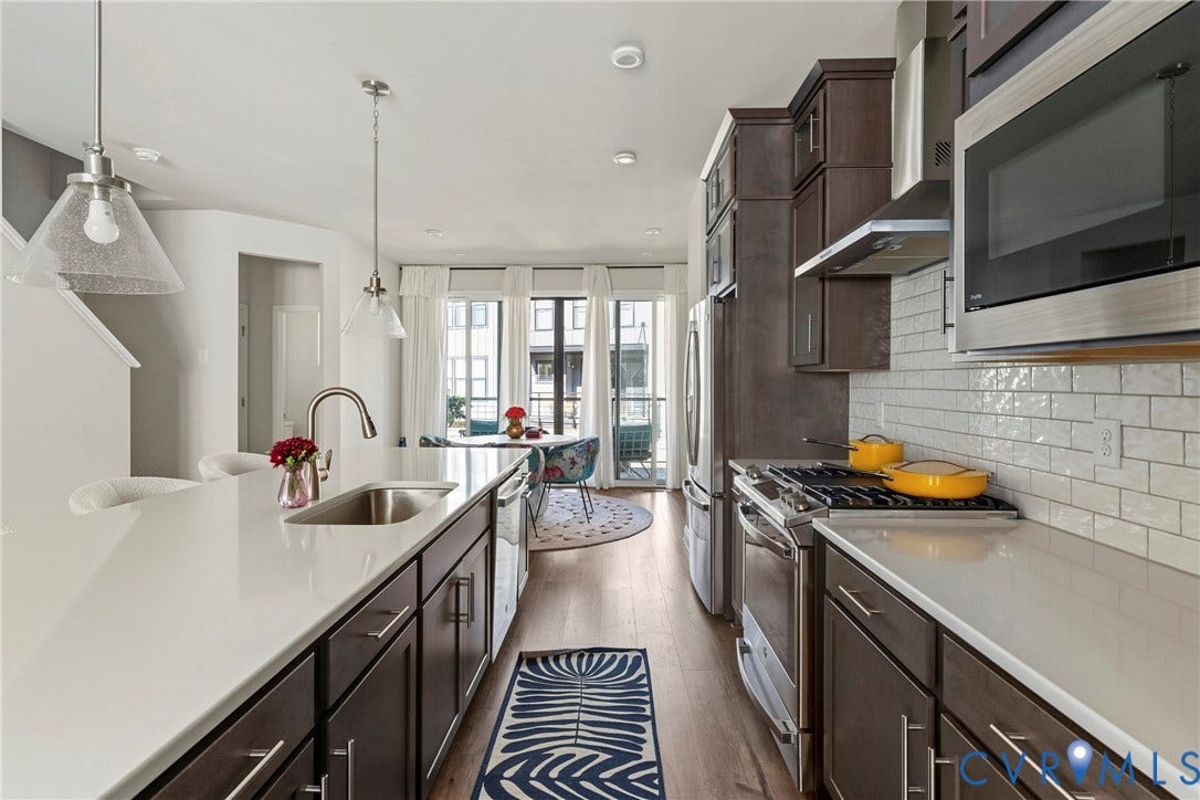Contemporary kitchen featuring a large island with an undermount sink, stainless steel appliances, dark wood-finish cabinetry, and white subway tile backsplash