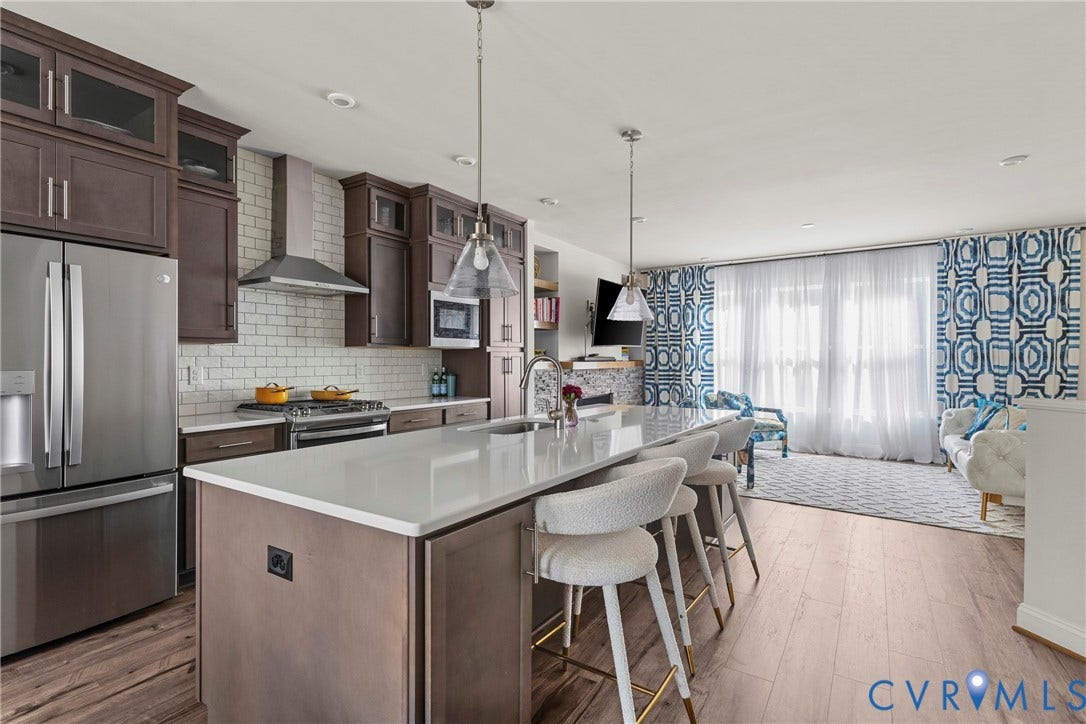 Spacious kitchen featuring an expansive island with a light-toned countertop, stainless steel appliances, and wood-finish flooring