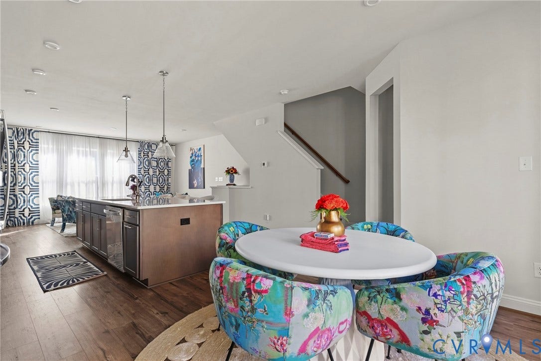 Open-concept living area featuring wood-finish flooring, a kitchen island with pendant lighting, and abundant natural light from large windows