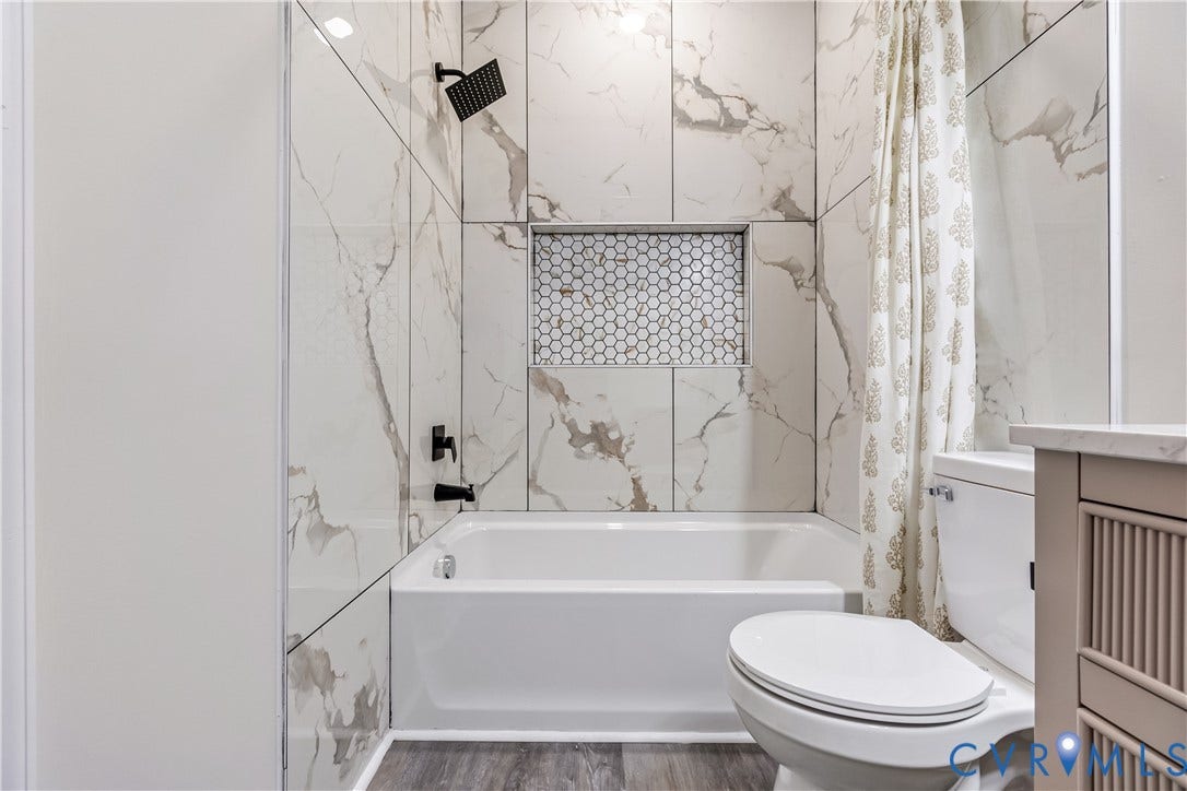 Bathtub and shower with floor-to-ceiling tile surround, recessed niche with hexagonal tile, matte black fixtures, and wood-finish flooring