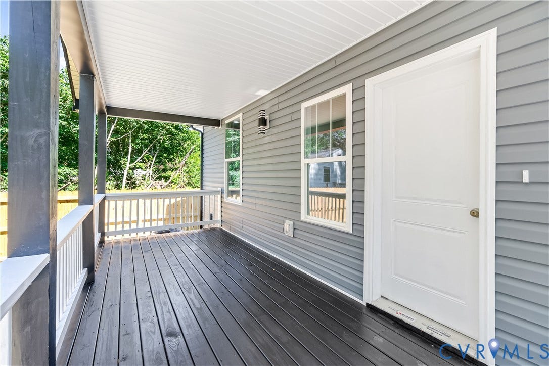 Covered porch with wood-finish flooring, white railing, and gray siding