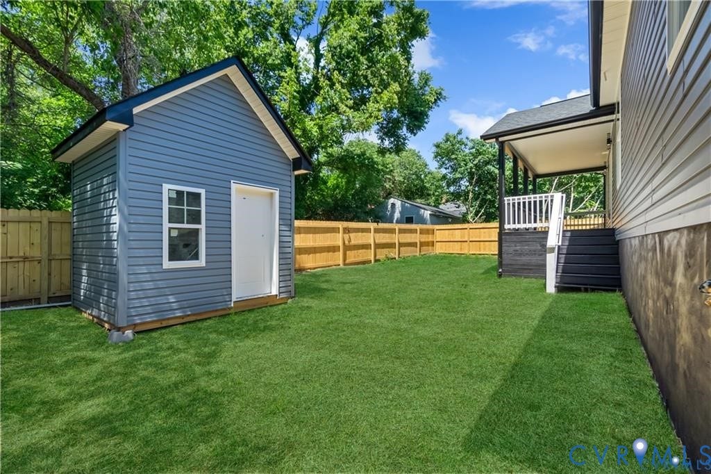 Expansive lawn with a wooden privacy fence, featuring a covered rear patio with exterior steps and a separate utility shed