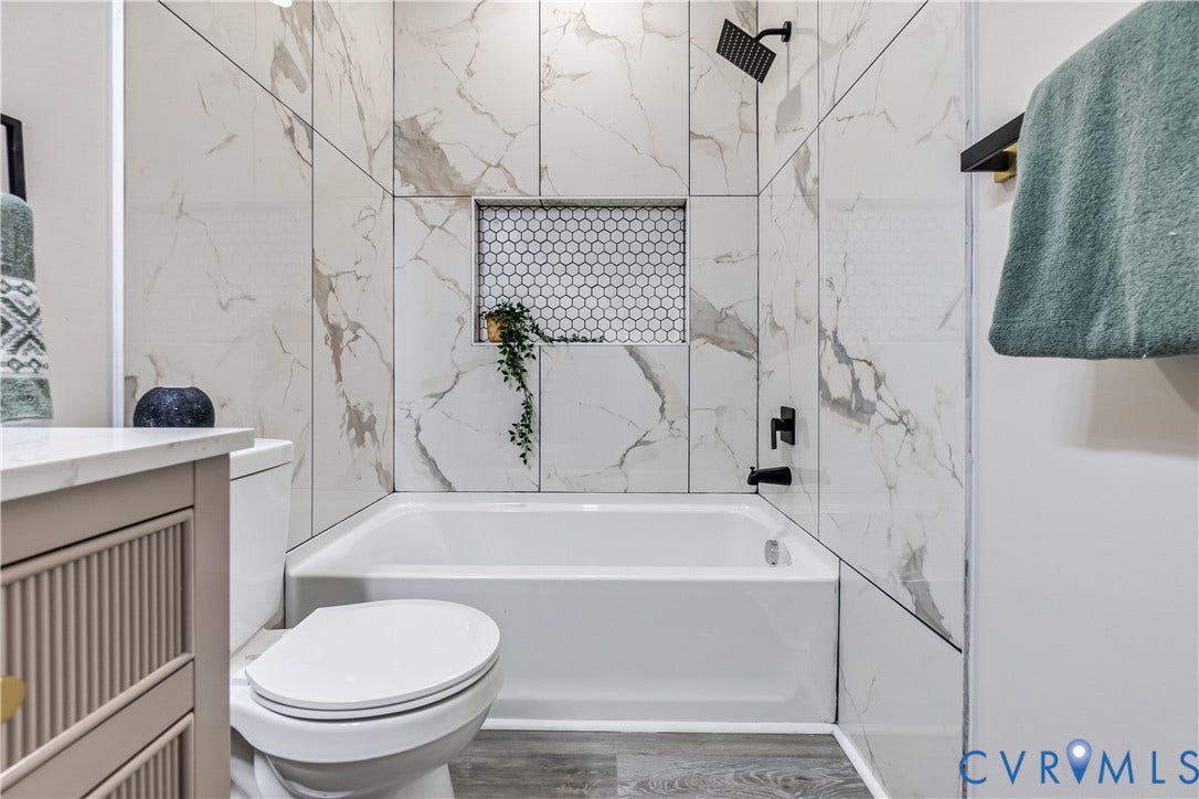 Bathtub with surrounding marble-finish tile, recessed niche with honeycomb tile, and matte black fixtures