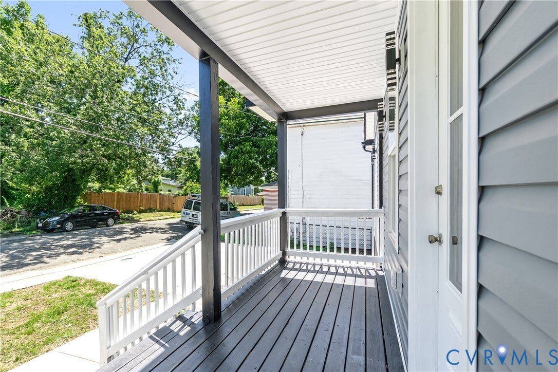 Covered porch with wood-finish flooring, white railing, and grey siding